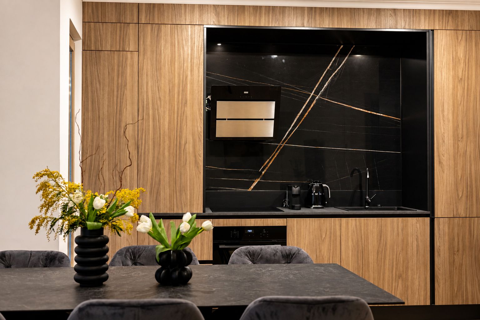 A modern kitchen with a built-in oven, a coffee maker, and a black backsplash.