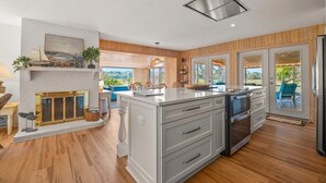 A modern kitchen with a large island, wooden flooring, and a view of the outdoors. - 864 Sabal Court - Beautiful Marsh Views (Fripp Island)