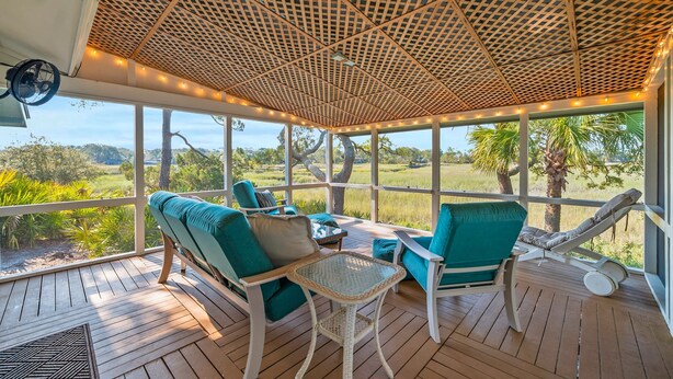 A covered outdoor seating area with chairs and a table, overlooking a natural landscape. - 864 Sabal Court - Beautiful Marsh Views (Fripp Island)