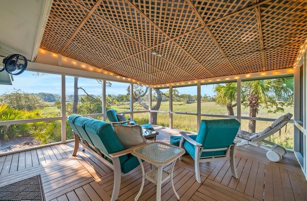 A covered outdoor seating area with chairs and a table, overlooking a natural landscape. - 864 Sabal Court - Beautiful Marsh Views (Fripp Island)