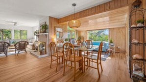 A spacious room with a dining table surrounded by chairs, a fireplace, and large windows offering a view of the outdoors. - 864 Sabal Court - Beautiful Marsh Views (Fripp Island)