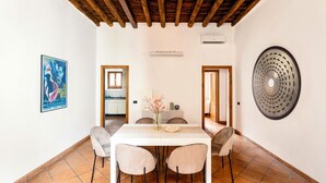 Un'area pranzo con un tavolo bianco, quattro sedie, un vaso con fiori e un elemento decorativo a parete.