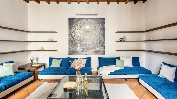 Un soggiorno moderno con un quadro grande, divani blu, un tavolino in vetro e travi in legno al soffitto.