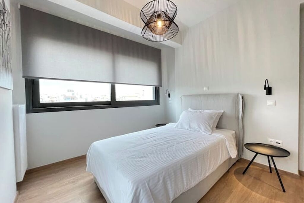 Et soveværelse med seng, et vindue, et lille bord og en lampe monteret på væggen.
