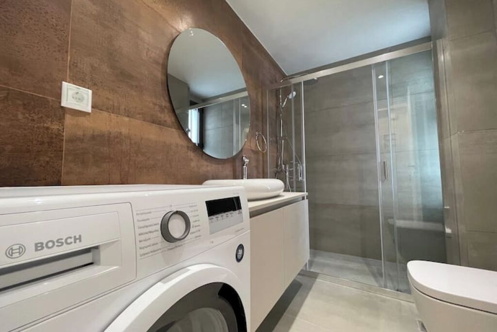 Une salle de bain moderne équipée d’un lave-linge Bosch, d’une douche à parois de verre et de toilettes.