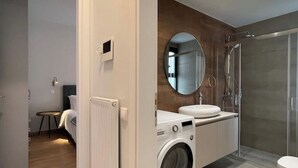 Een moderne badkamer met een ingebouwde wasmachine, een ronde spiegel en een douchecabine van glas.