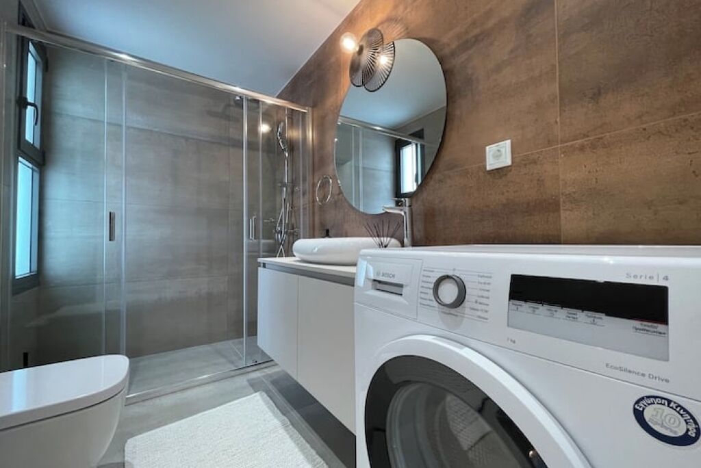 A modern bathroom with a glass shower enclosure, a Bosch washing machine, and a large mirror.