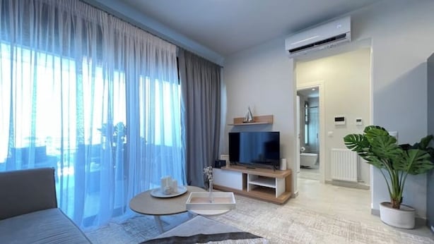 Ett modernt hotellrum med ett stort fönster, en platt-TV, en soffa, ett soffbord och en krukväxt.