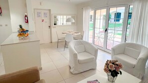 A hotel room with a dining area, white furniture, a fire extinguisher, and a view through the glass doors. - Sunny Village Vilamoura (Loulé)