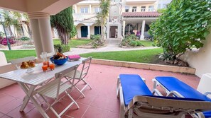An outdoor patio with a table set for breakfast, a view of a building with a tiled roof, and a garden area. - Sunny Village Vilamoura (Loulé)