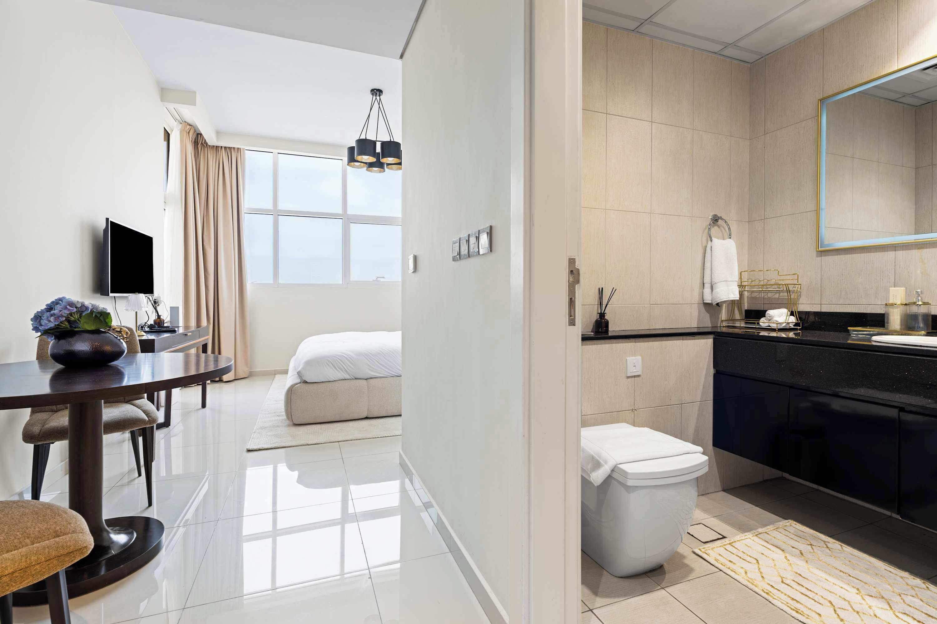 Quarto de hotel com área de refeições, cama, banheiro com espelho grande e televisão.
