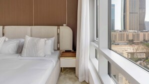 A hotel room with a large bed, a wooden headboard, a window with a city view, and a small wooden nightstand. - Luxury 2BR in Downtown Dubai, Near Burj Khalifa (Downtown)