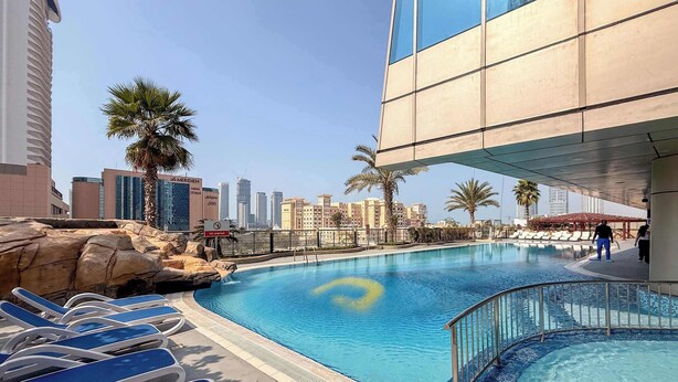 A swimming pool with lounge chairs, a rock formation, and a city skyline in the background. - Stylish 2BR w Study and City Views (Dubai Marina)