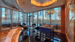 A modern room with large windows, a foosball table, and a unique ceiling design. - Stylish 2BR w Study and City Views (Dubai Marina)