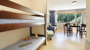 Ein Zimmer mit Etagenbett, kleinem Tisch und Stühlen sowie einem Fenster mit Blick auf Grünflächen.