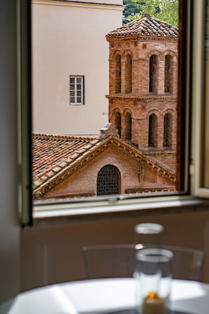 Une vue par la fenêtre sur un bâtiment en briques, doté de fenêtres en arc de cercle et d’un toit recouvert de tuiles.