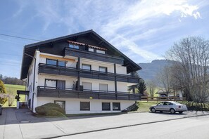 Un immeuble de deux étages avec un balcon, une voiture garée devant et un ciel dégagé.