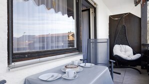 Un coin repas avec une table dressée pour deux personnes, un fauteuil suspendu et une vue par la fenêtre.