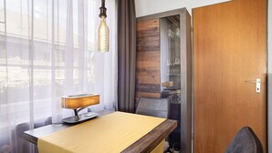 Une chambre d’hôtel avec une table en bois, une lampe, une chaise, une porte et une fenêtre avec des rideaux.
