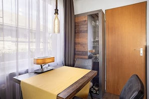 Ein Hotelzimmer mit einem Holztisch, einer Lampe, einem Stuhl, einer TĂŒr und einem Fenster mit VorhĂ€ngen.
