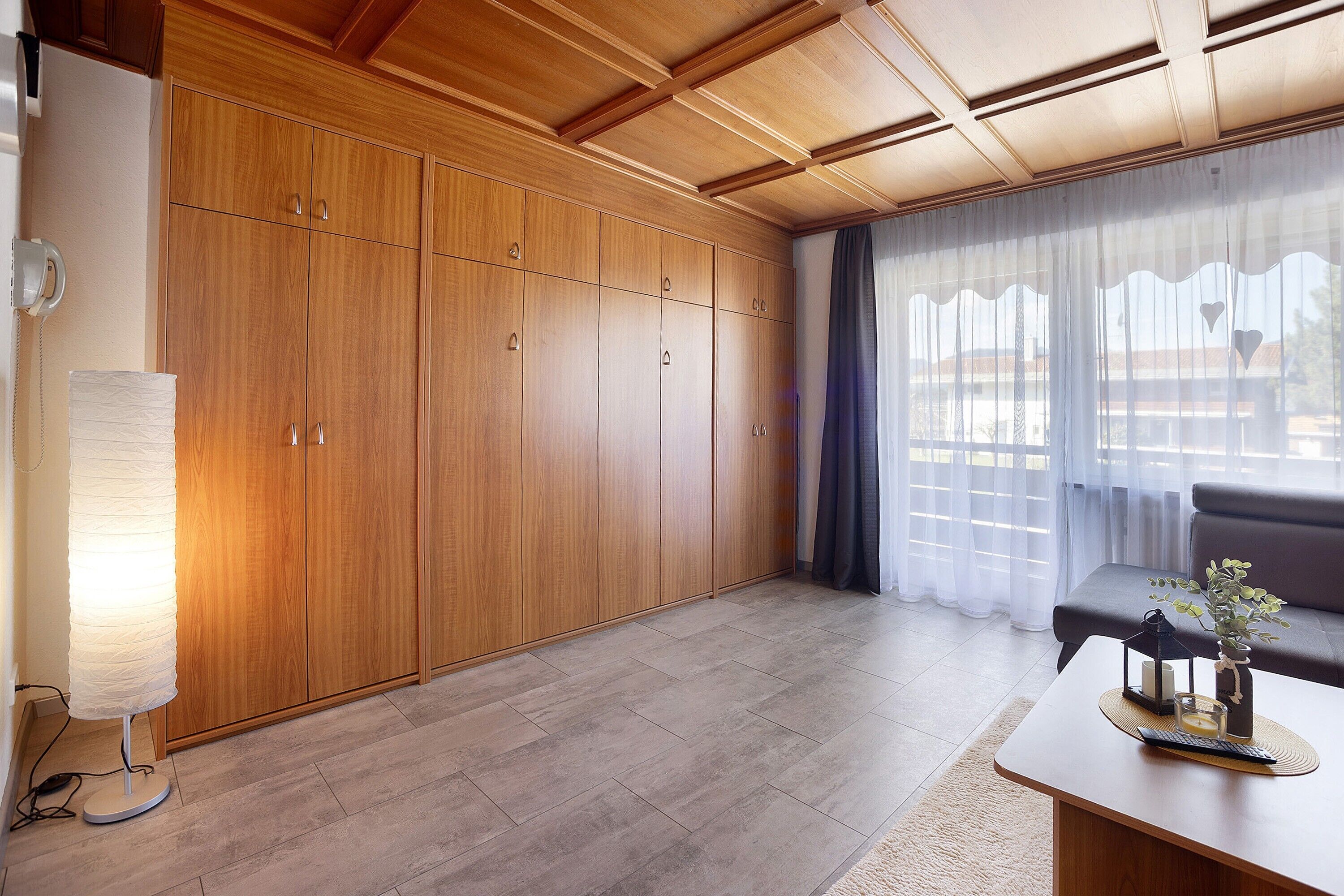 Een kamer met houten kasten, een bank, een tafel met decoratieve objecten en een lamp.