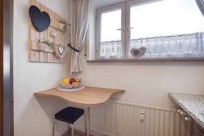 Une cuisine avec une table en bois, un panier de fruits et une fenêtre ornée de rideaux en dentelle.