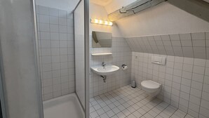 Une salle de bain avec des murs carrelés de carrelage blanc, une douche, un lavabo et des toilettes.