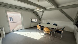 Une pièce avec une grande table et des chaises, un ventilateur de plafond et une fenêtre.