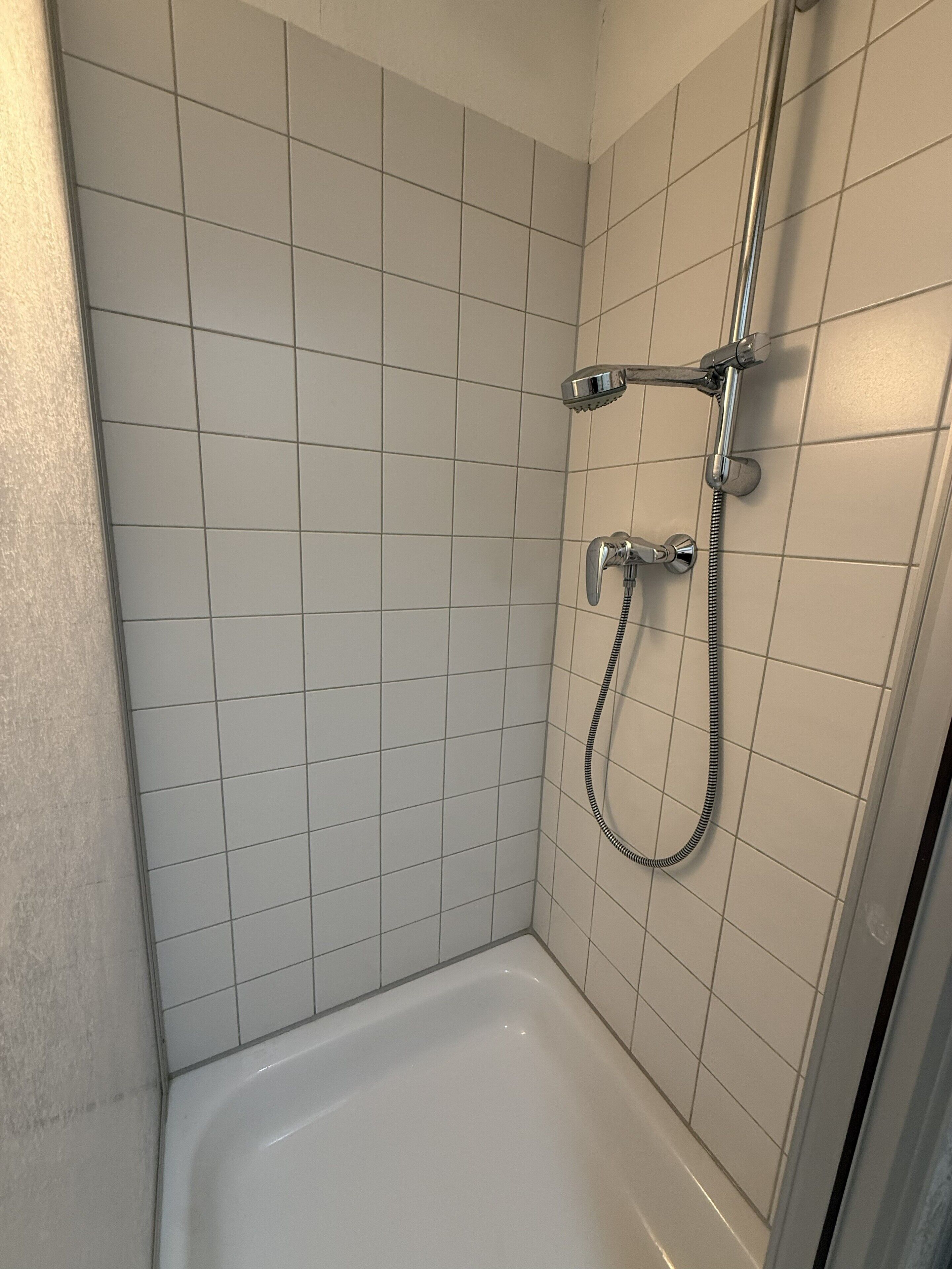 A shower with a handheld showerhead and a fixed showerhead, a bathtub, and tiled walls.