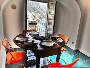 Ein Essbereich mit einem Tisch für zwei Personen, Stühlen und Blick auf eine Berglandschaft durch ein Fenster.