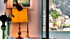 Quarto com cama, luminária e janela com vista para uma cidade costeira.