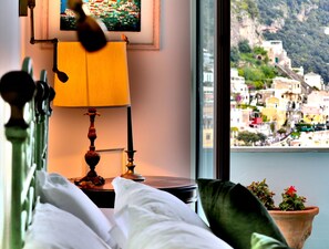 Ein Zimmer mit Bett, Lampe und Fenster mit Blick auf eine Küstenstadt.