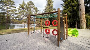 Ein Spielplatz mit einer Seilnetz-Klettervorrichtung, Schaukeln und roten, runden Elementen.