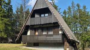 Ein traditionelles Holzhaus mit steilem Dach, einem Balkon und einem umgebenden Wald.