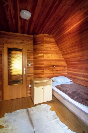 Ein Zimmer in einer Holzhütte mit einem Bett, einem Holzschrank, einer Tür mit Glasfenster und einem weißen Fellteppich.