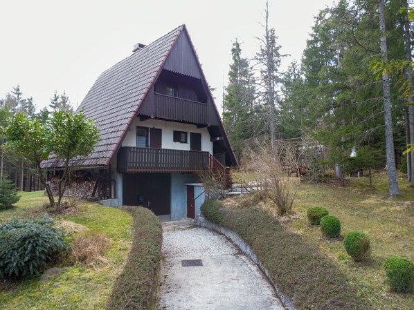 Ein zweistöckiges Haus mit geneigtem Dach, einem Balkon und einer Zuwegung aus Kies zum Eingang.