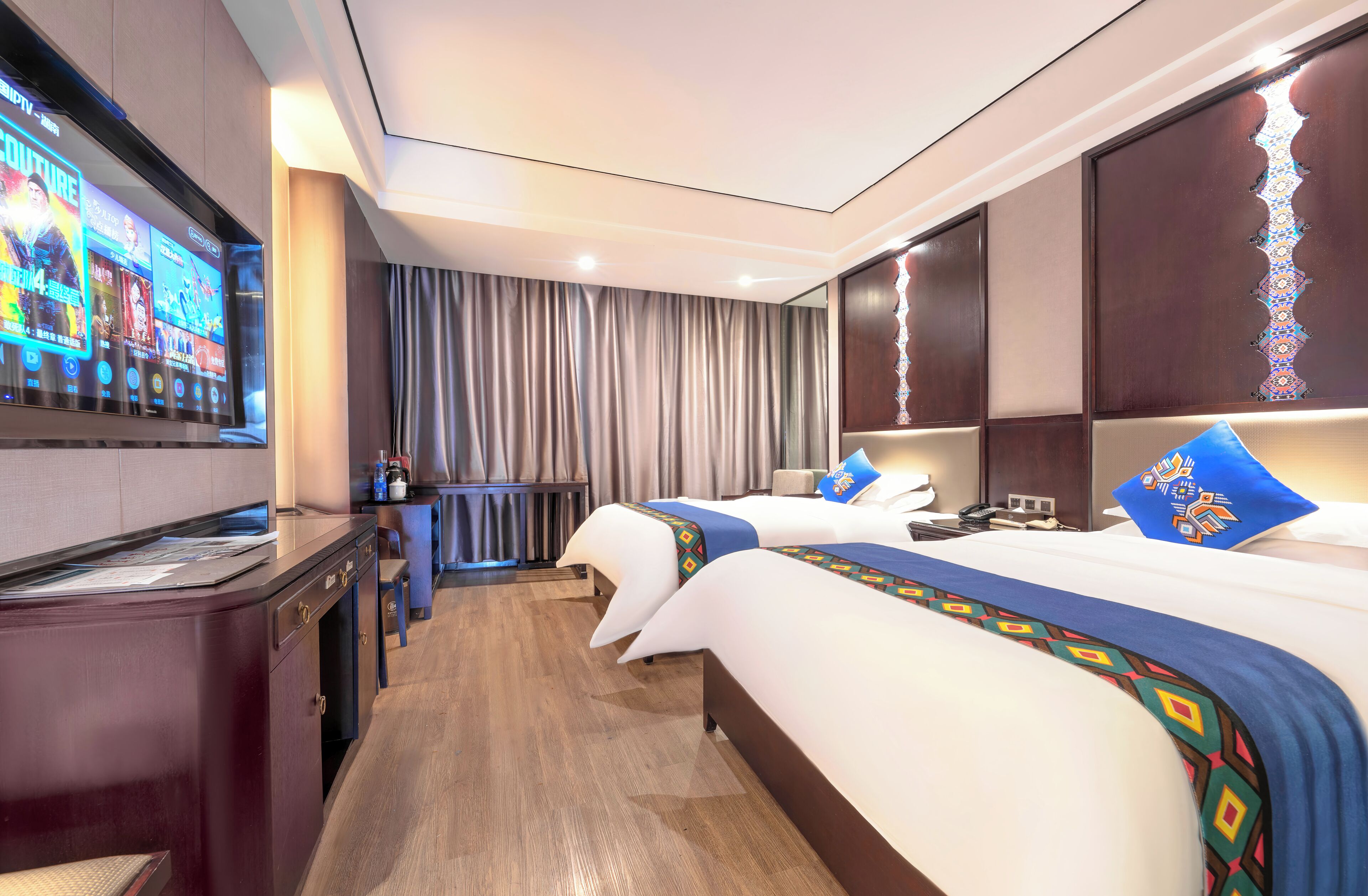 A hotel room with two beds, a TV, a desk, and a minibar.