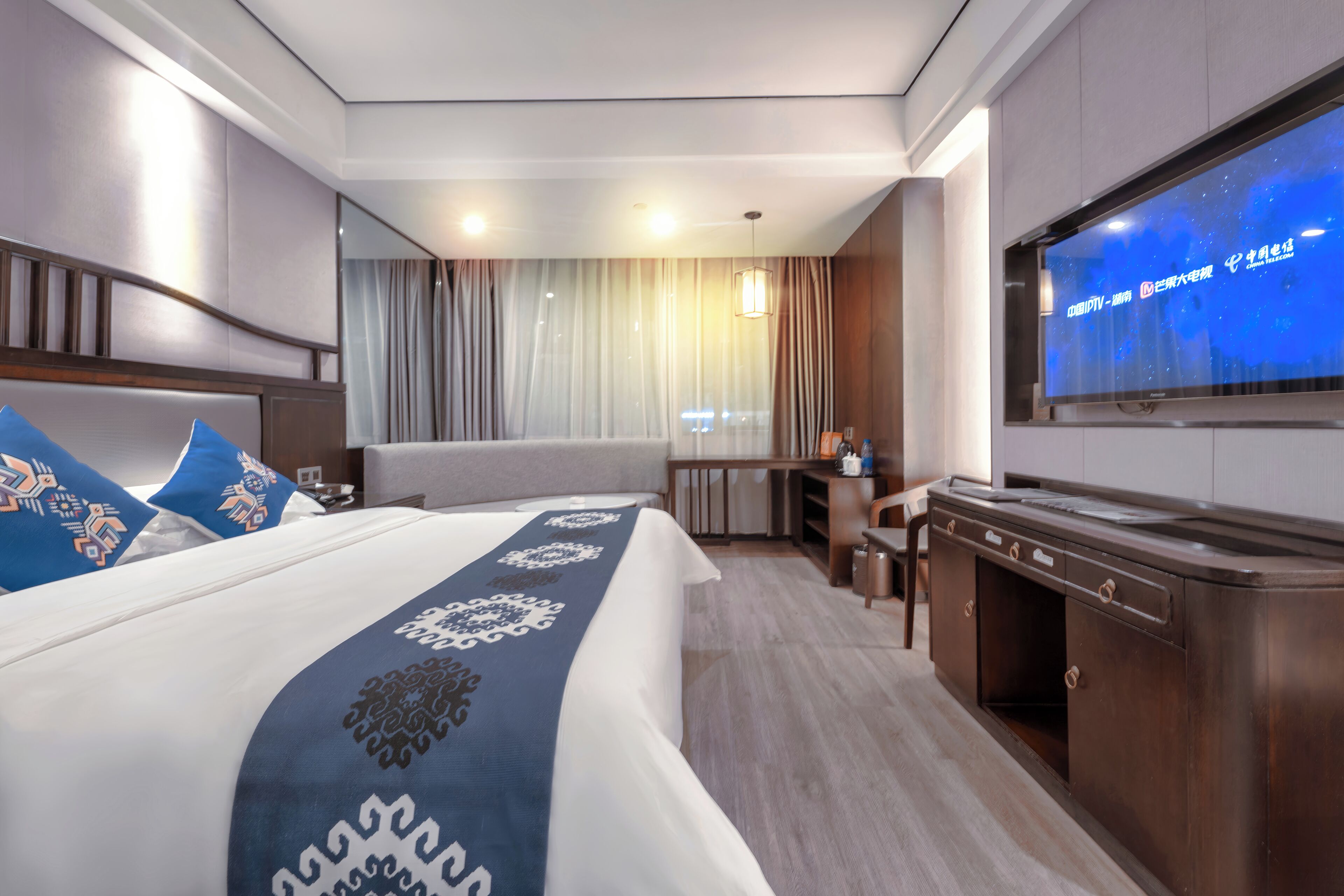 A hotel room with a large bed, a desk, a television, and a view of the cityscape.