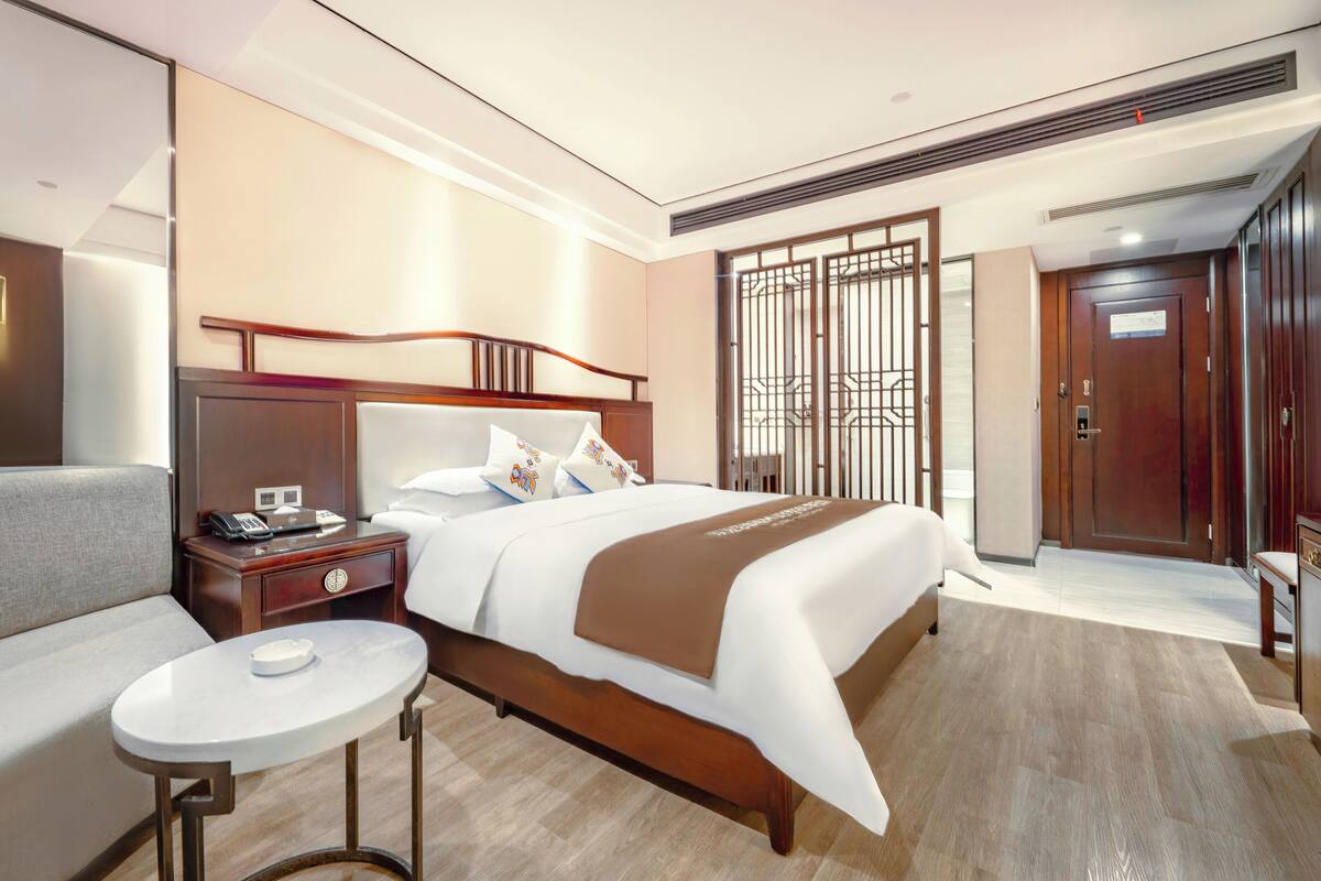 Een hotelkamer met een bed, nachtkastje, lamp en een klein rond tafeltje.