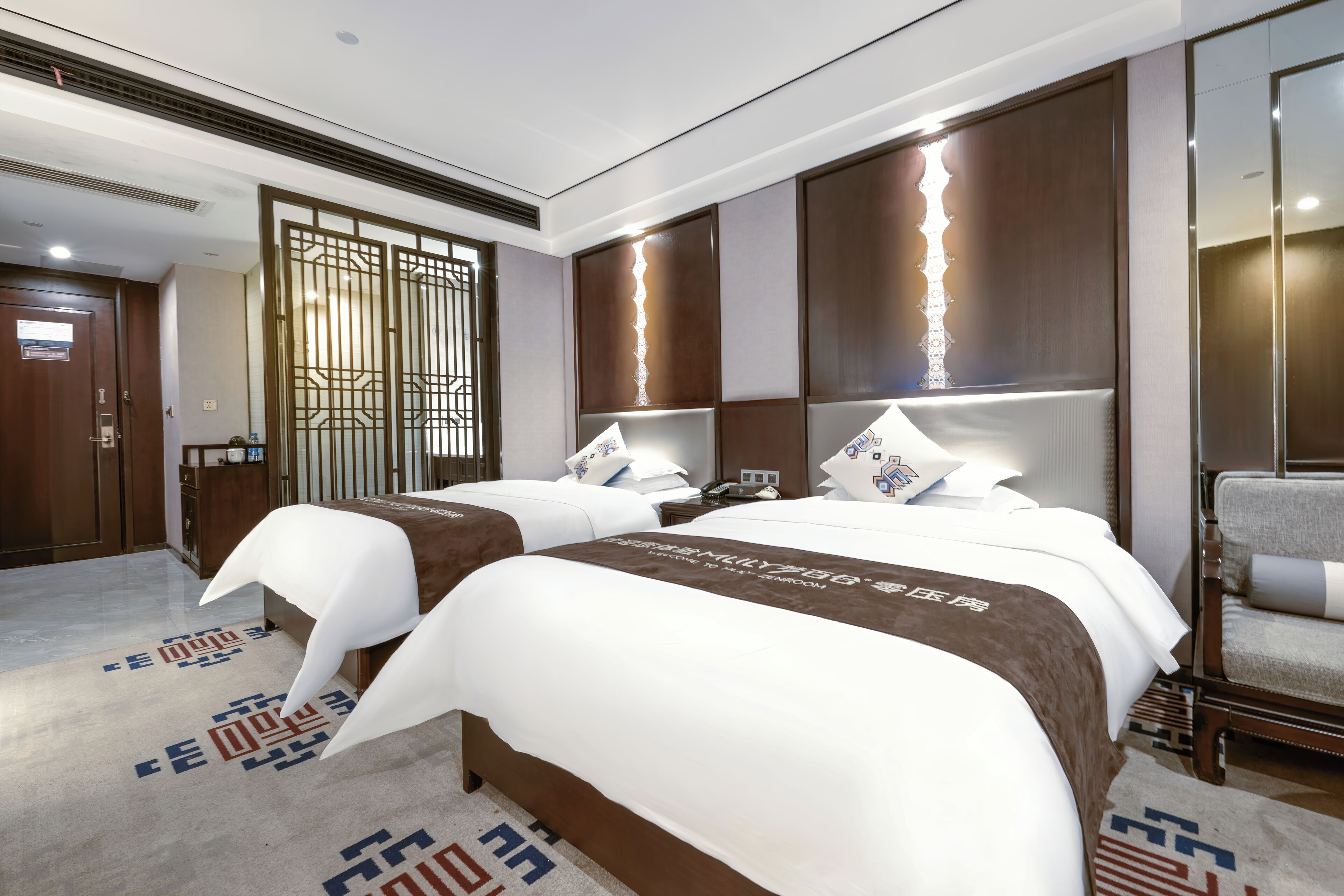 A hotel room with two beds, a large window, a wooden door, and a small desk.