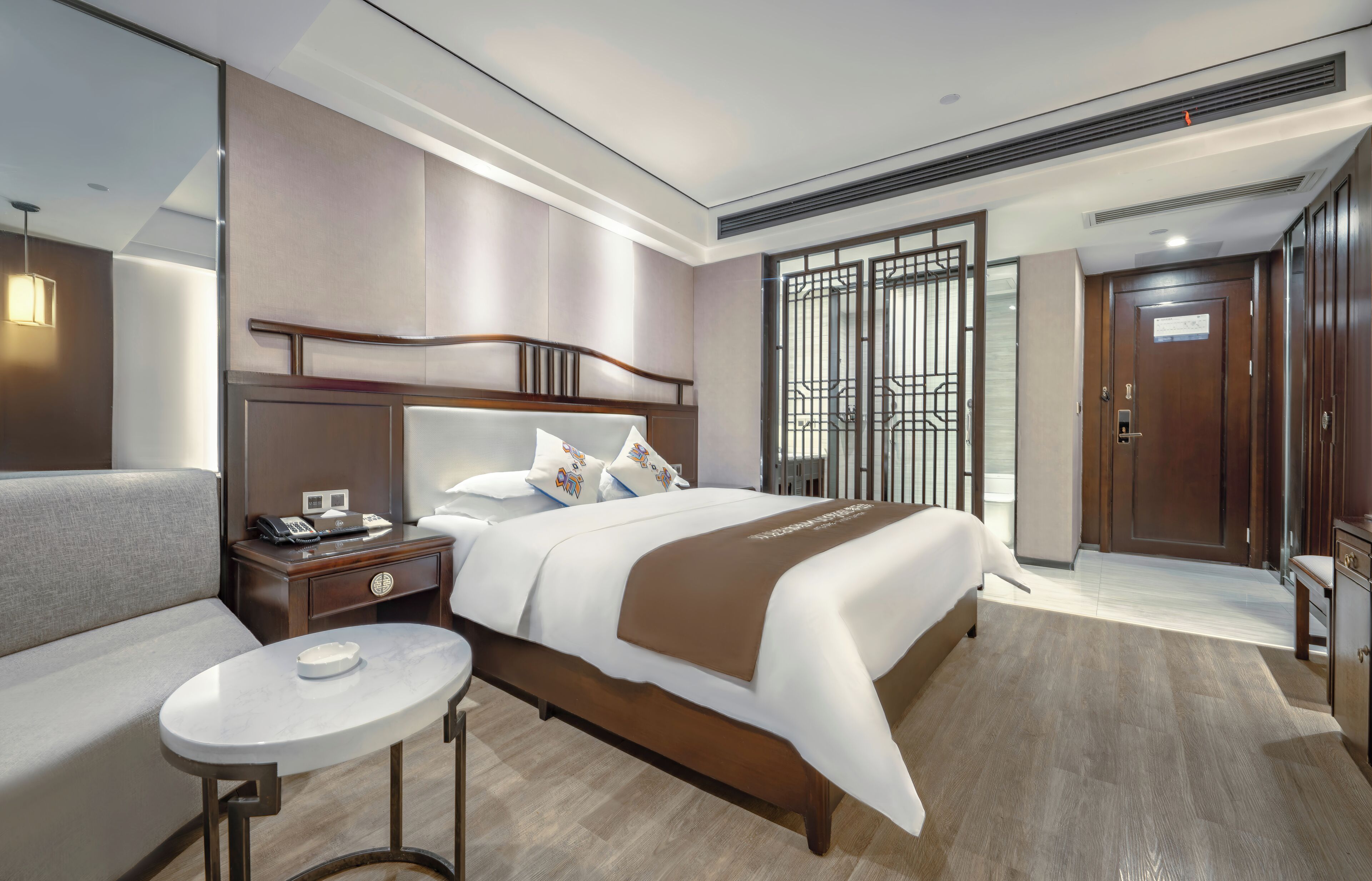 A modern hotel room with a large bed, bedside table, and a small round table.