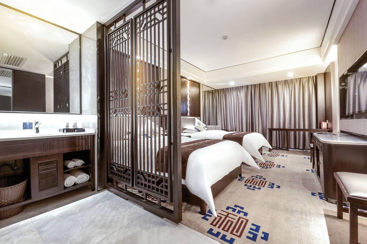 Een hotelkamer met een grote spiegel, een bed, een bureau en een badkamer met wastafel en handdoekhouder.