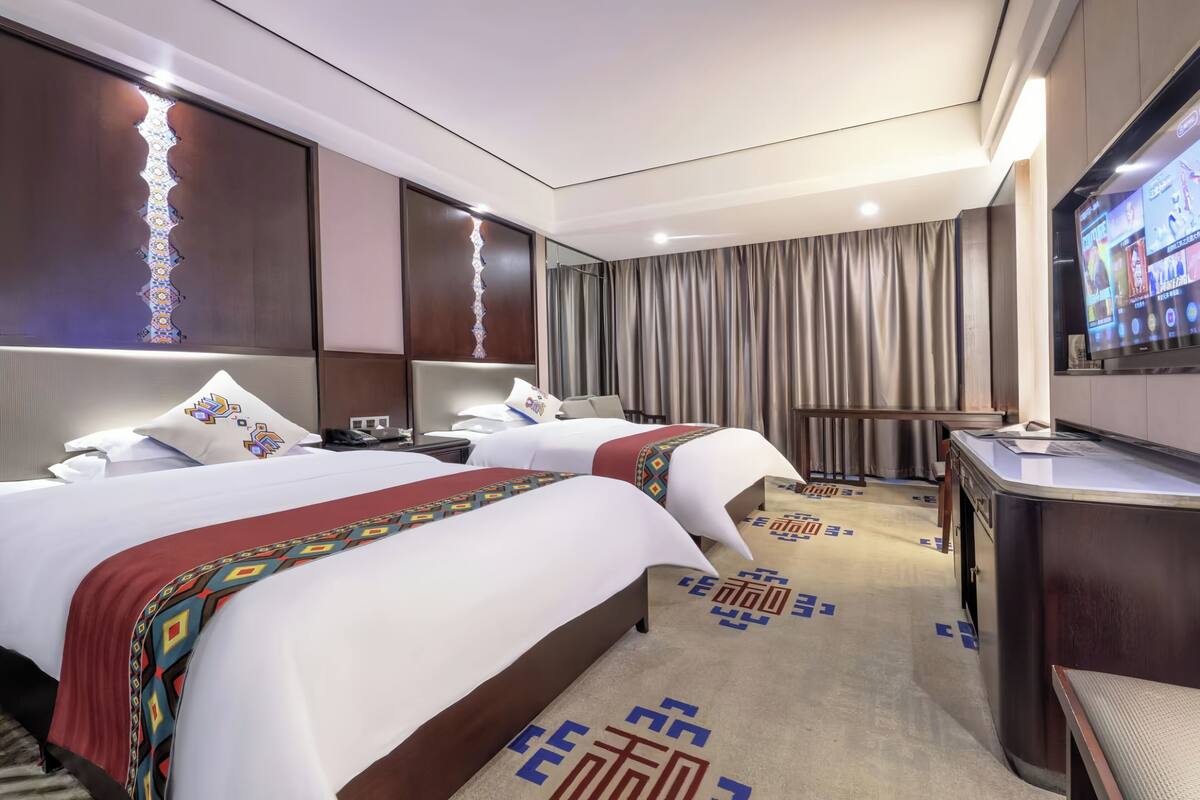 Een hotelkamer met twee bedden, een televisie, een bureau en een groot raam met gordijnen.