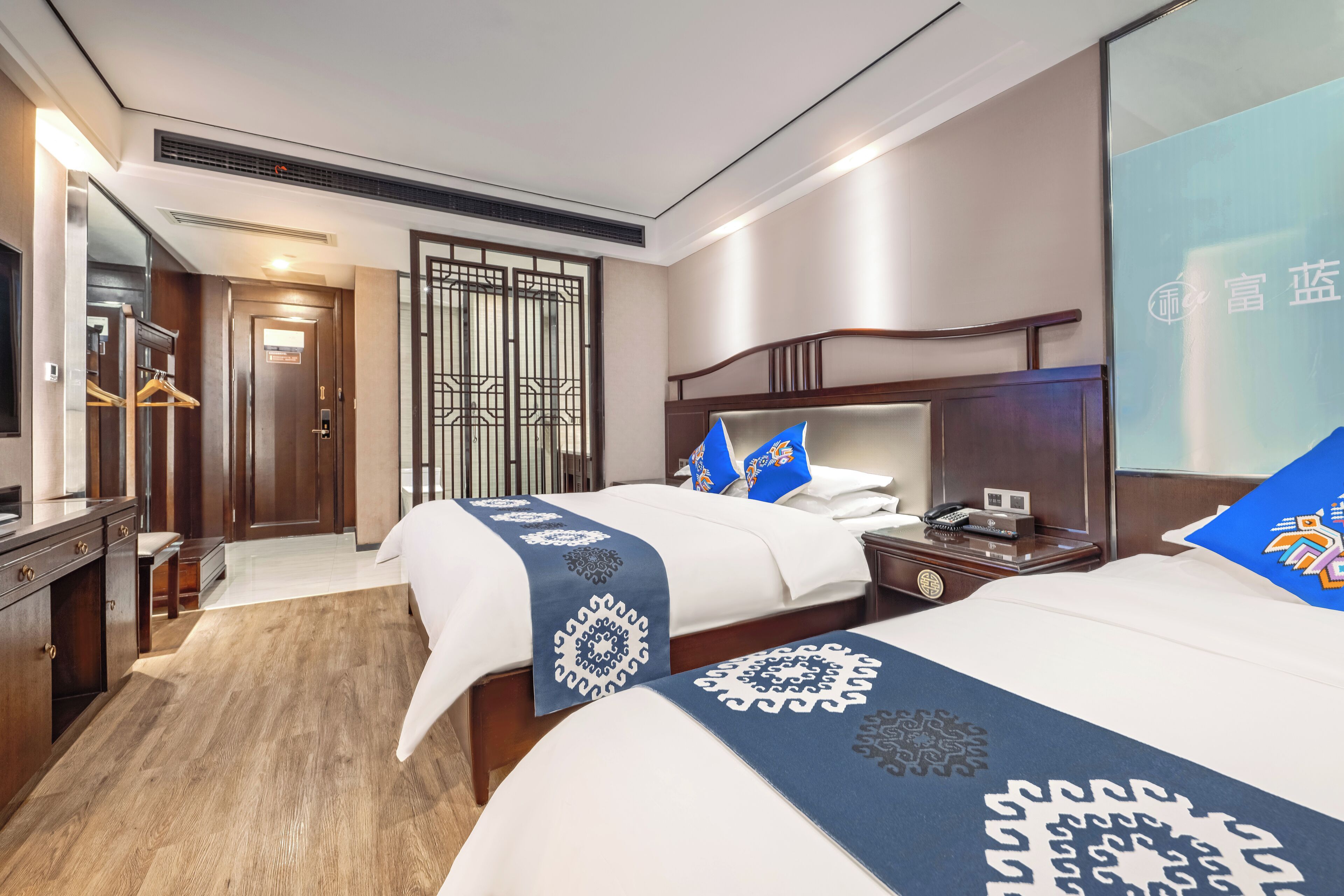 A hotel room with two beds, a desk, a wardrobe, and a large mirror.