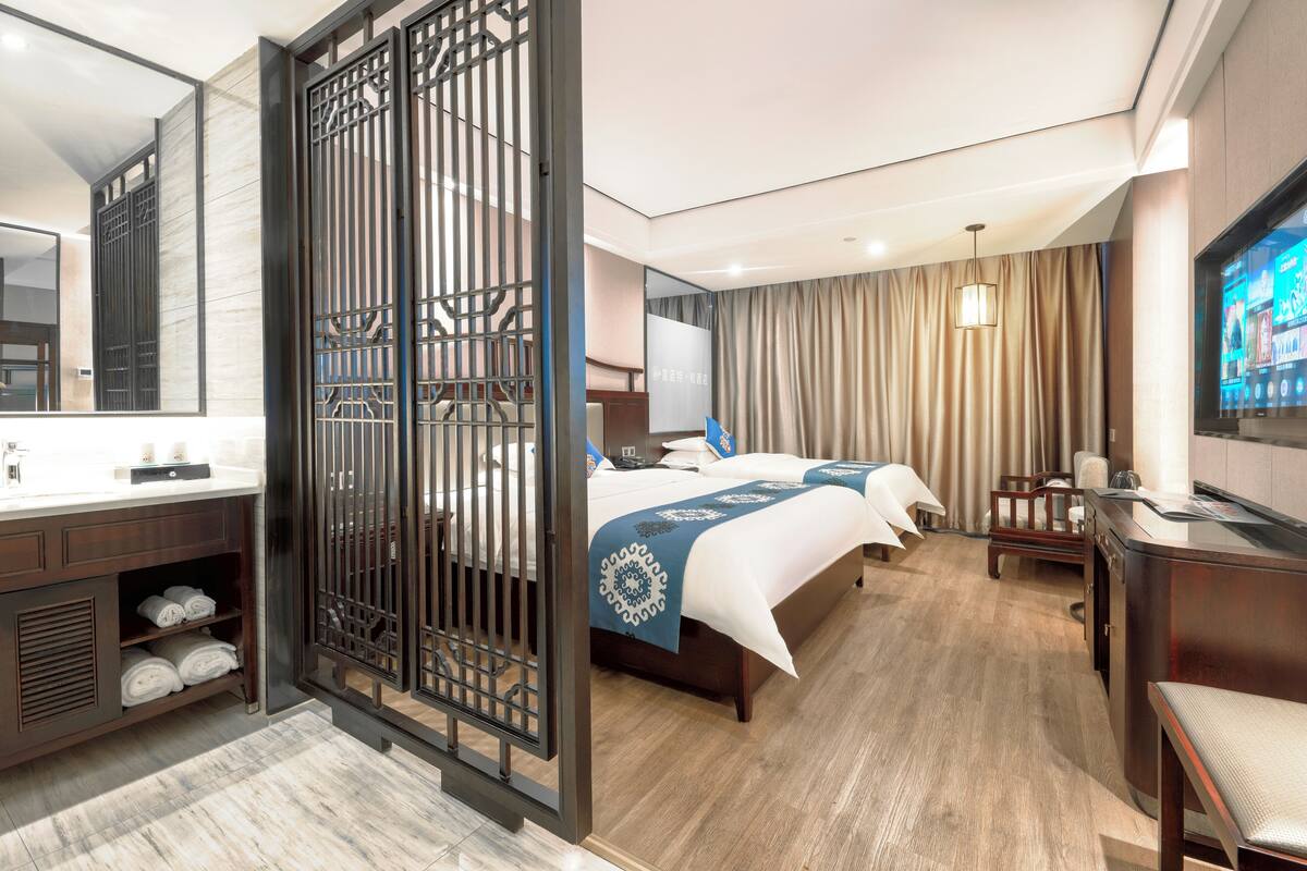 Een hotelkamer met een groot bed, een bureau, een televisie en een badkamer met spiegel en wastafel.