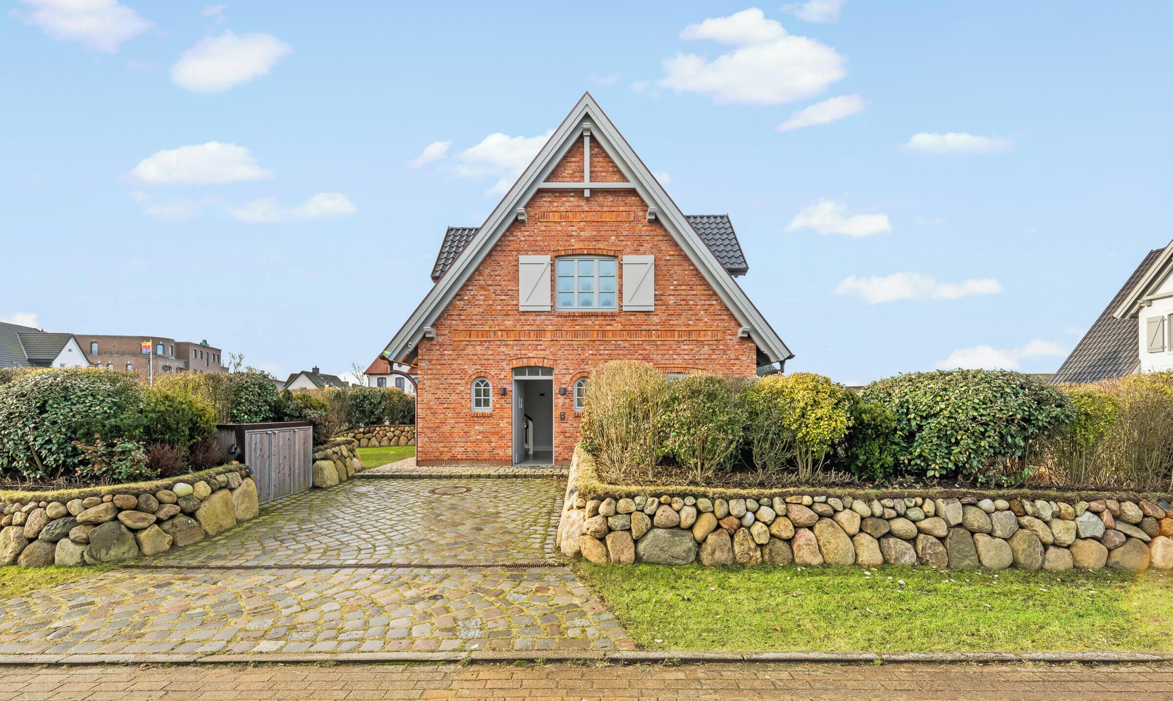 A brick house with a stone pathway leading to the entrance, surrounded by greenery and a stone wall.