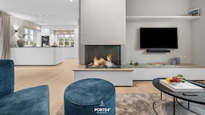 Una sala de estar moderna con chimenea, un televisor de pantalla plana y un comedor con un libro y fruta.