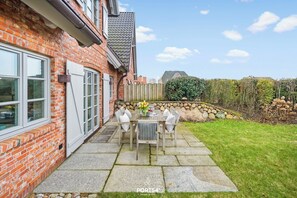 Une maison en briques avec un patio, une table et des chaises, et un mur en pierre.