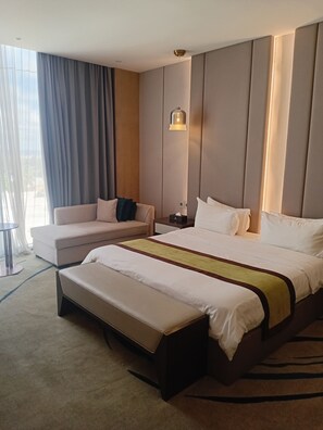 A hotel room with a large bed, a sofa, a bench, a bedside table, and a window with curtains. - Marigold Hotel  (Windhoek)