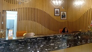 Un mostrador de recepción con encimera de mármol, paneles de pared de listones de madera e iluminación colgante geométrica.